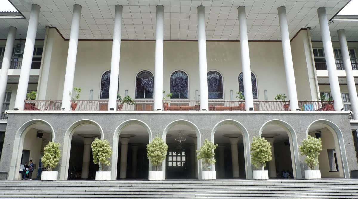 Fasad depan Balairung Universitas Gadjah Mada dengan deretan pilar putih tinggi, jendela lengkung, dan tangga di bagian depan